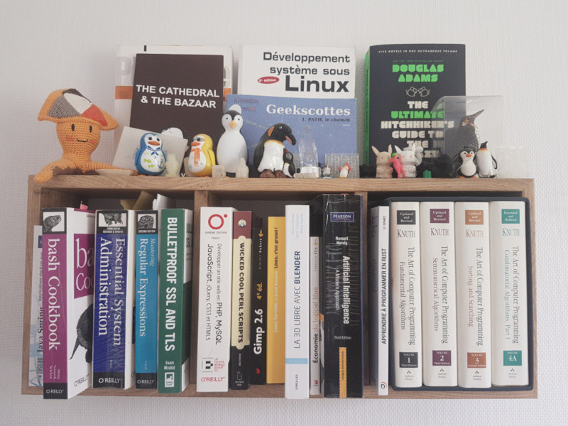 étagère contenant une vingtaine de livres en relation avec l'informatique et décorée avec des goodies en lien avec l'écosystème du logiciel libre